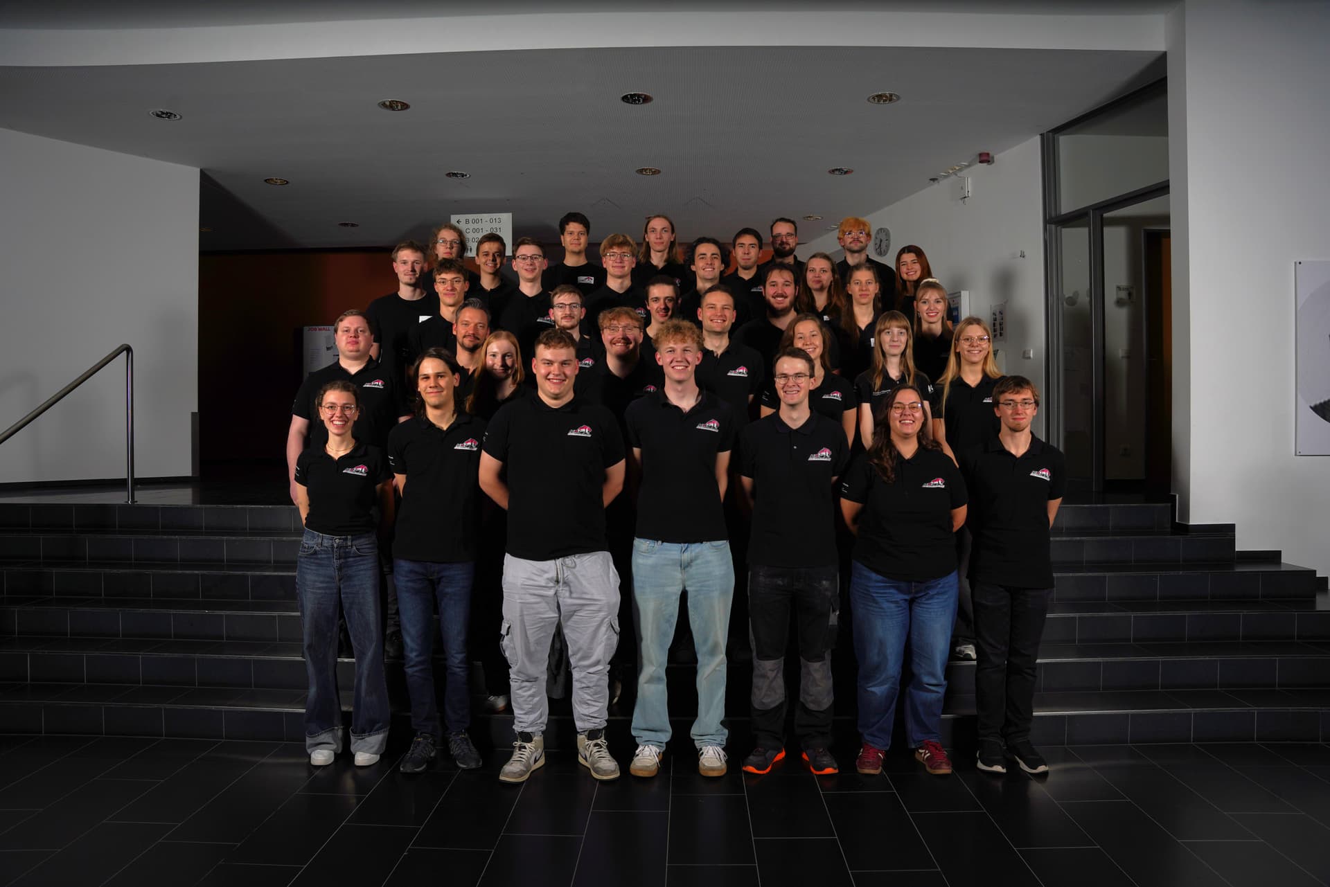 Teammitglieder 2025/26, lächelnd auf Treppenstufen der Hochschule Hof in Teamkleidung